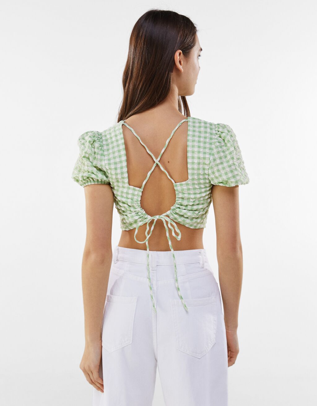 Woman wears Gingham blouse with tied detail at the back and white jeans and faces away from camera