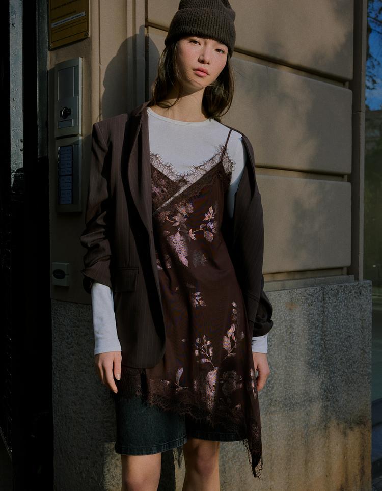 Set de rochie maro cu dantelă florală, tricou alb, jachetă maro și căciulă tricotată.